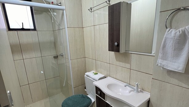 A modern bathroom with a glass shower enclosure, a white toilet, a sink with a mirror above, and a towel hanging on a rack. - Family apartment with great comfort and a great location in Toledo, Paraná. (Toledo)