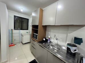 A compact kitchen with a sink, microwave, and a small window.