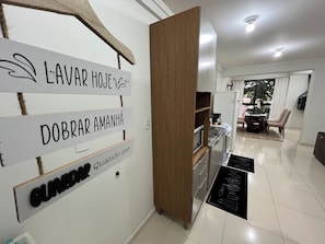 Cocina moderna con un mueble de madera, un refrigerador blanco y una encimera negra. Hay un cartel en la pared con texto en un idioma extranjero.