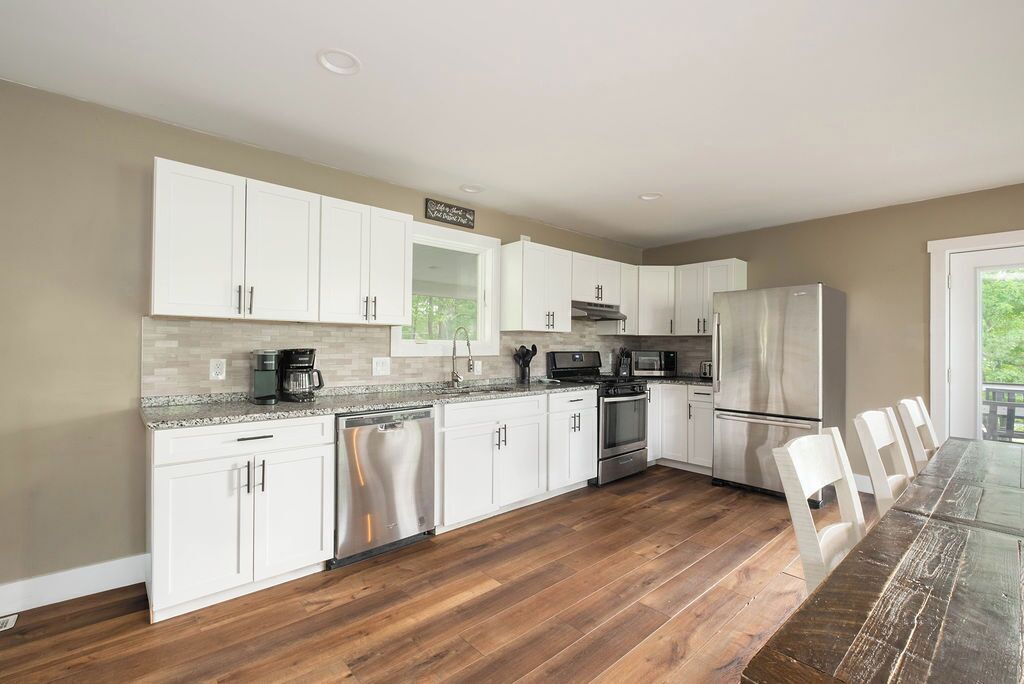 A modern kitchen with white cabinets, a stainless steel refrigerator, and a wooden dining table.