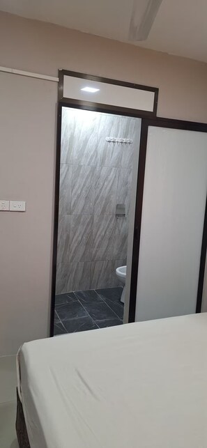 A hotel room with a bed, a bathroom with a toilet and a shower, and a door leading to another room. - Raj Vista Residence (Nadi)