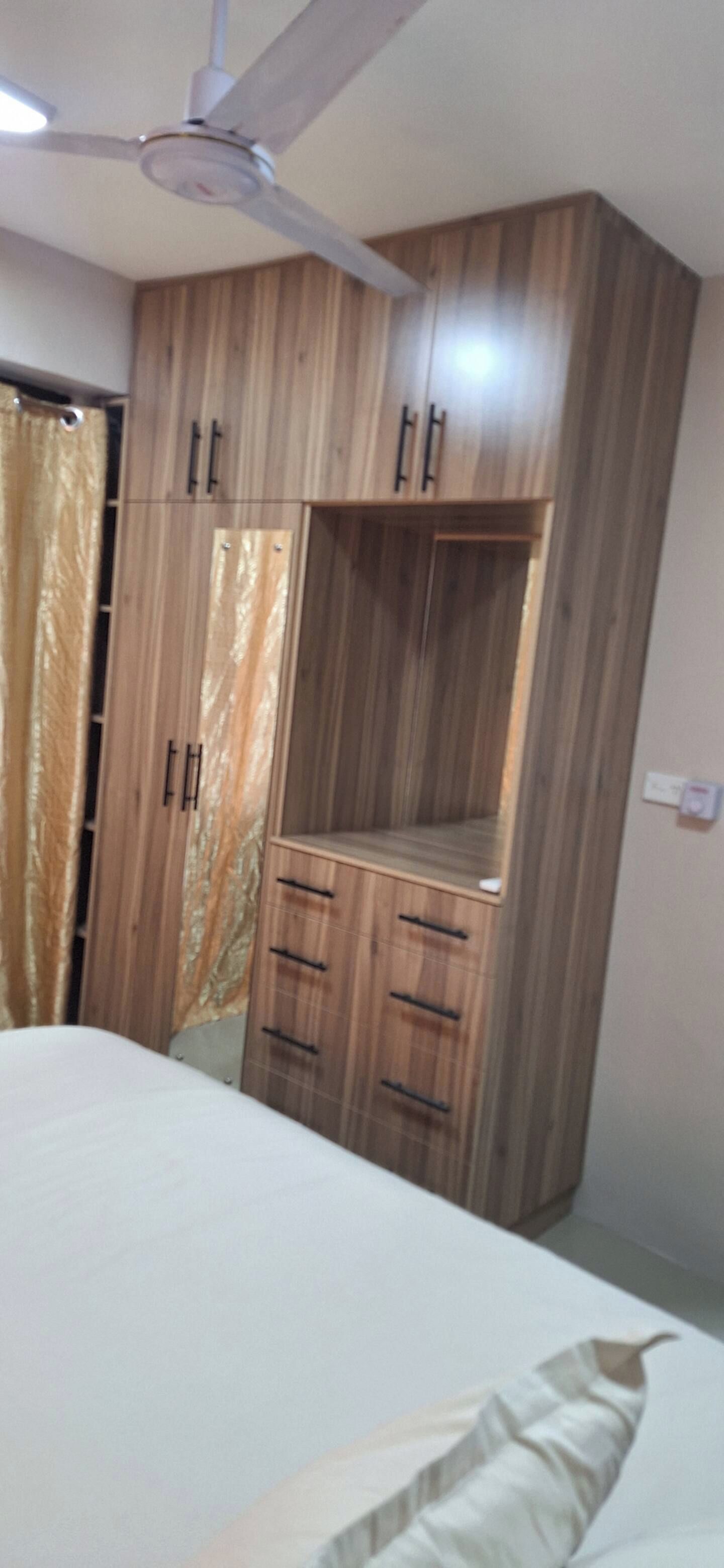 Quarto com cama, guarda-roupa de madeira e ventoinha no teto.