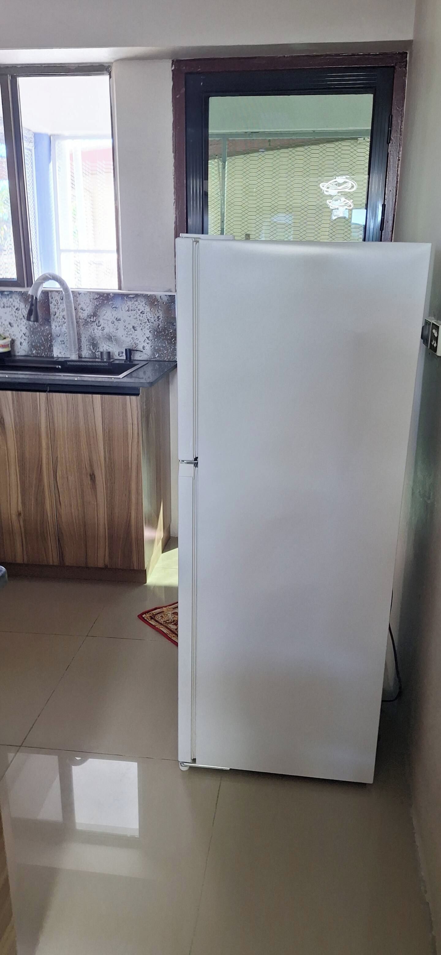 Una cocina con un refrigerador blanco, una encimera de madera y un ventanal con vistas a una cerca verde.