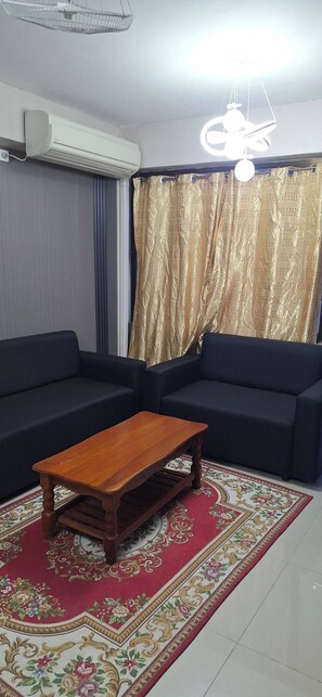A living room with two dark sofas, a wooden coffee table, a patterned rug, and a ceiling fan. - Raj Vista Residence (Nadi)