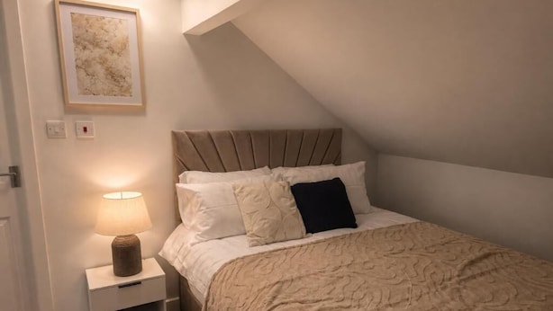 Un dormitorio con cama, mesita de noche y lámpara fijada a la pared.