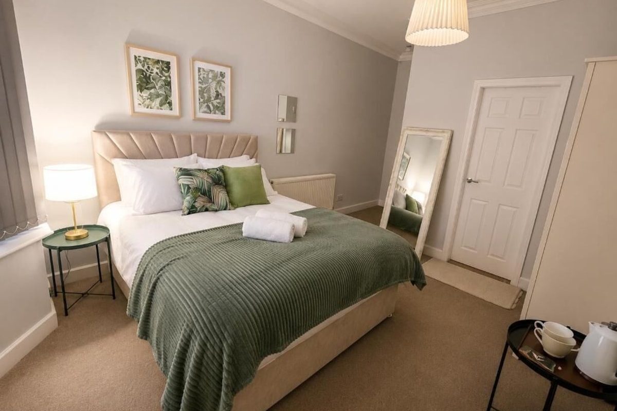 A neatly arranged bedroom with a bed, bedside tables, a mirror, and a door.