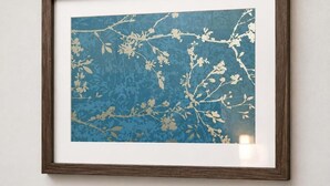 Una obra de arte enmarcada con fondo azul y motivos florales blancos.