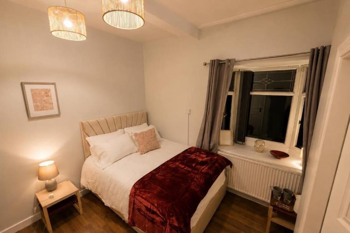 A bedroom with a bed, bedside lamp, window with curtains, and a radiator.