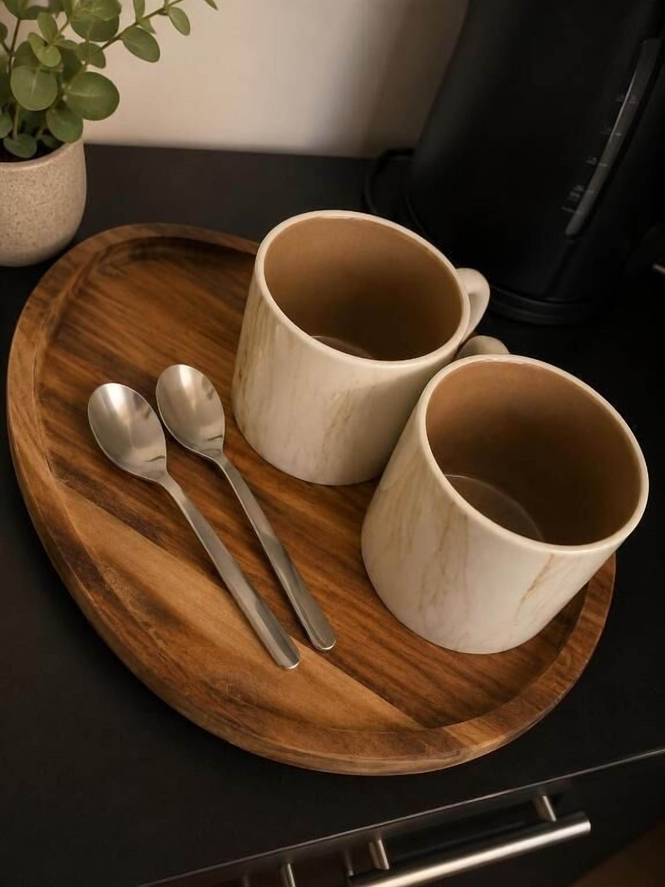Una bandeja de madera con dos tazas blancas de cerámica y dos cucharas sobre una encimera de cocina.