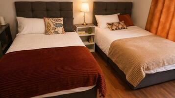 A hotel room with two beds, each with a different colored blanket, a bedside table with a lamp, and a nightstand with a cup.