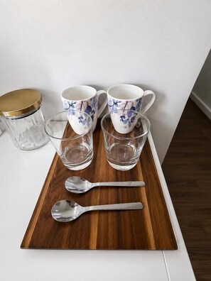 A wooden tray with three white cups with blue floral patterns, two clear glasses, and a metal spoon. - Mauldeth Road Guest House (Manchester)