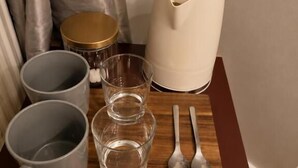 Una bandeja de madera con una cafetera, dos tazas, dos vasos y dos cucharas.