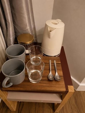 A wooden tray with a coffee maker, two mugs, two glasses, and two spoons.