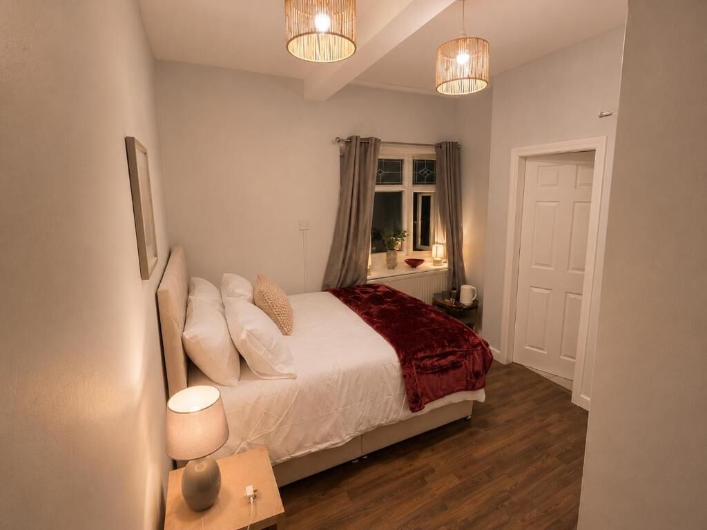 A bedroom with a bed, bedside lamp, window with curtains, and a door.