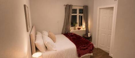 A bedroom with a bed, bedside lamp, window with curtains, and a door.