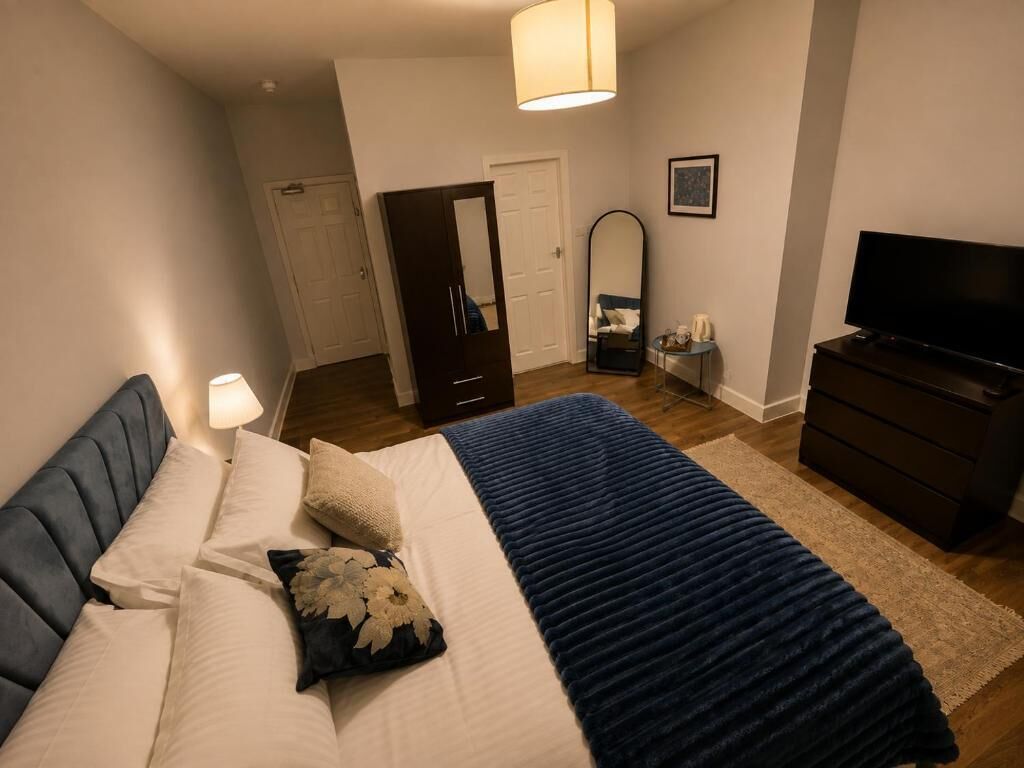 Una camera da letto con un letto, una cassettiera, una televisione, uno specchio e una porta.
