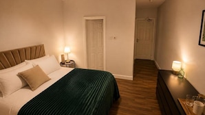 Un dormitorio con cama, mesitas de noche, cómoda y una puerta que da a otra habitación.
