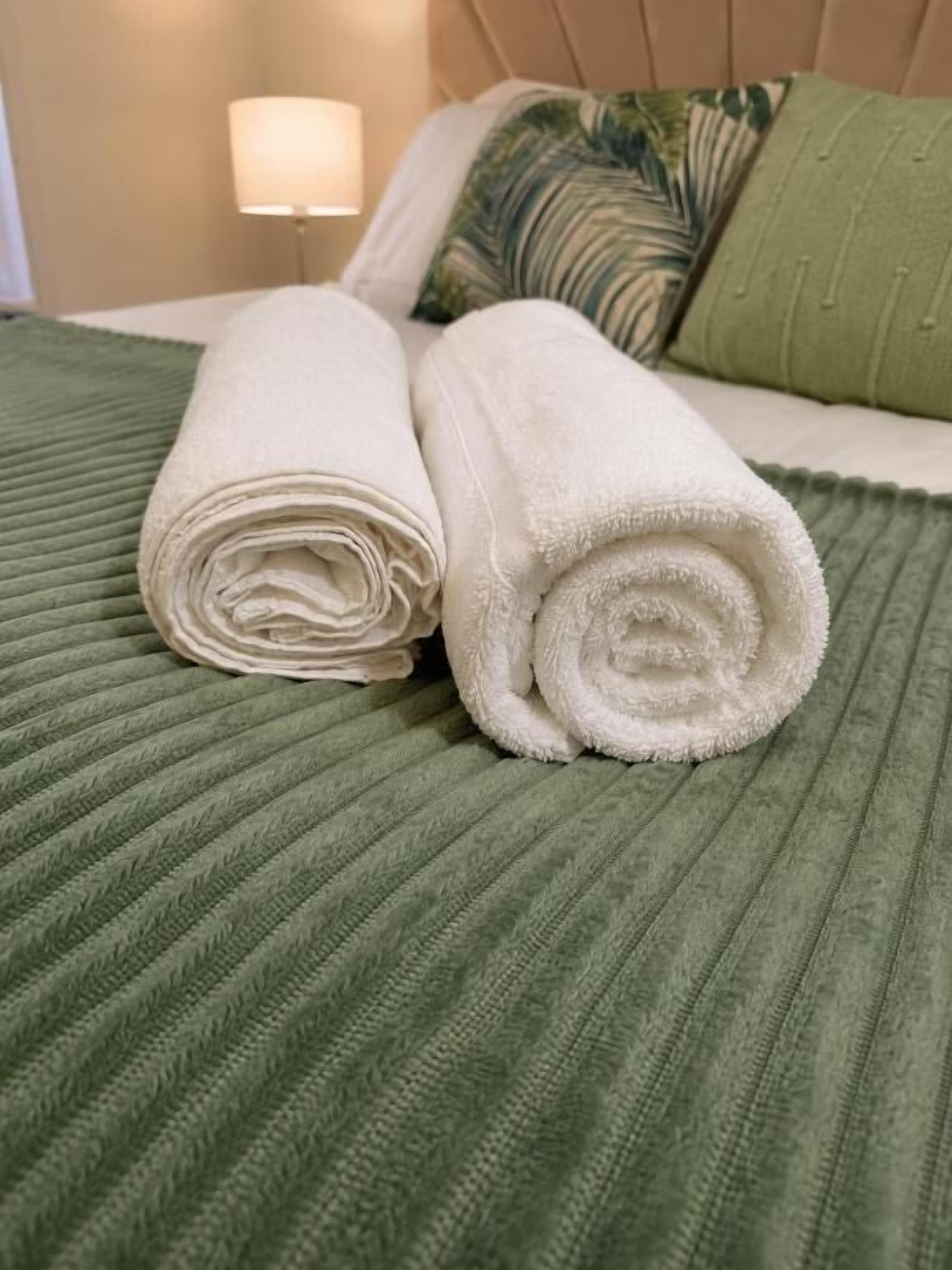 A neatly made bed with rolled white towels and a green textured bedspread.