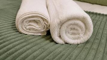 A neatly made bed with rolled white towels and a green textured bedspread.