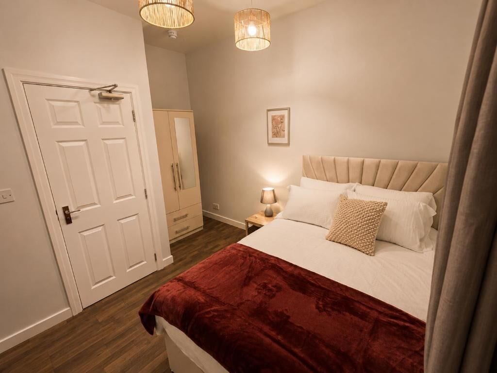 A bedroom with a bed, a nightstand, a lamp, a door, and a wardrobe.