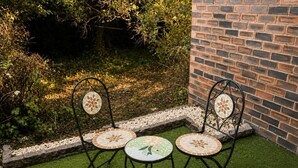 Un patio con dos sillas de metal y una mesa, rodeado por un muro de ladrillo y follaje.
