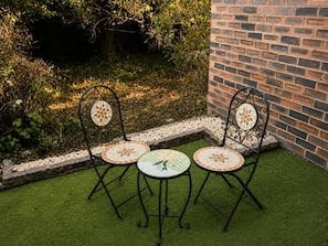 A patio with two metal chairs and a table, surrounded by a brick wall and greenery.