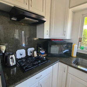 A kitchen with white cabinets, a gas stove, a toaster, a kettle, and a microwave.