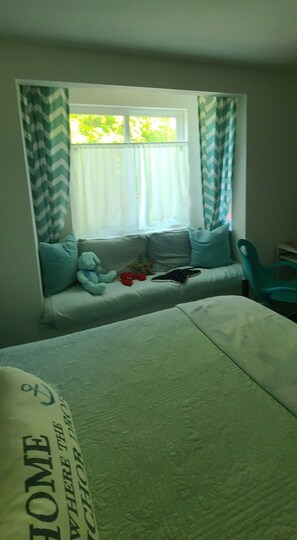 A room with a bed, a window with curtains, a sofa with cushions, and a chair.