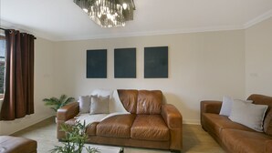A living room with a brown leather sofa, two side chairs, a coffee table, and a modern chandelier. There are three abstract paintings on the wall. - Leslie Lodge - Grampian Lettings (Inverurie)