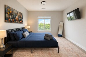 A bedroom with a bed, a nightstand, a lamp, a painting, a window, a mirror, and a TV. - Stylish 2BR | Balcony + UAB Access (Birmingham)