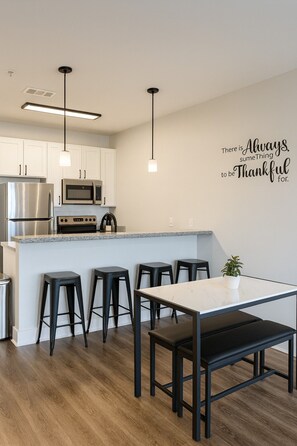 A modern kitchen with white cabinets, stainless steel appliances, a granite countertop, and black bar stools. - Stylish 2BR | Balcony + UAB Access (Birmingham)
