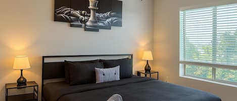 Un dormitorio con cama, dos mesitas de noche, ventilador de techo, ventana con persianas y una obra de arte en la pared.
