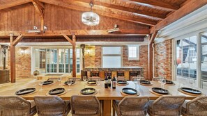 A spacious dining area with a long table set for a meal, featuring wicker chairs and a brick wall backdrop.