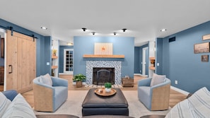 A living room with a fireplace, two armchairs, a coffee table, and a wooden door. - Private Ranch- Pool, Sauna, Outdoor Theater, & Gaming Barn (El Cajon)