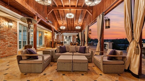 A covered outdoor seating area with wicker furniture and a brick wall.