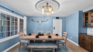 Comedor con mesa de madera, sillas, candelabro y decoración de cabeza de vaca en la pared.