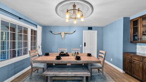 A dining room with a wooden table, chairs, a chandelier, and a wall-mounted cow head decoration.