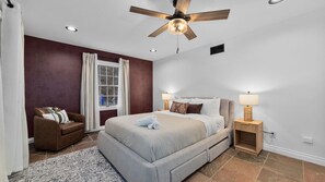 A bedroom with a bed, a nightstand, a ceiling fan, and a window with curtains.