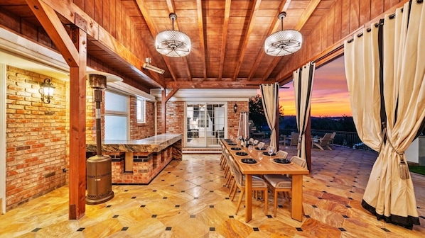 An indoor dining area with a brick wall, wooden ceiling, and a long table set for dining. - Private Ranch- Pool, Sauna, Outdoor Theater, & Gaming Barn (El Cajon)