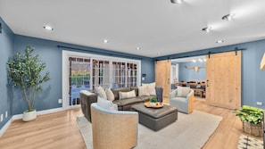 A modern living room with a sectional sofa, a coffee table, and a dining area visible through a glass door.