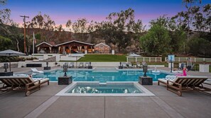 A swimming pool with lounge chairs, a wooden deck, and a house in the background.