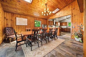 A wooden interior with a dining area, kitchen, and a large window with a view of greenery. - Eagle's Landing | Cozy, Pet-Friendly Getaway (Hammondsport)