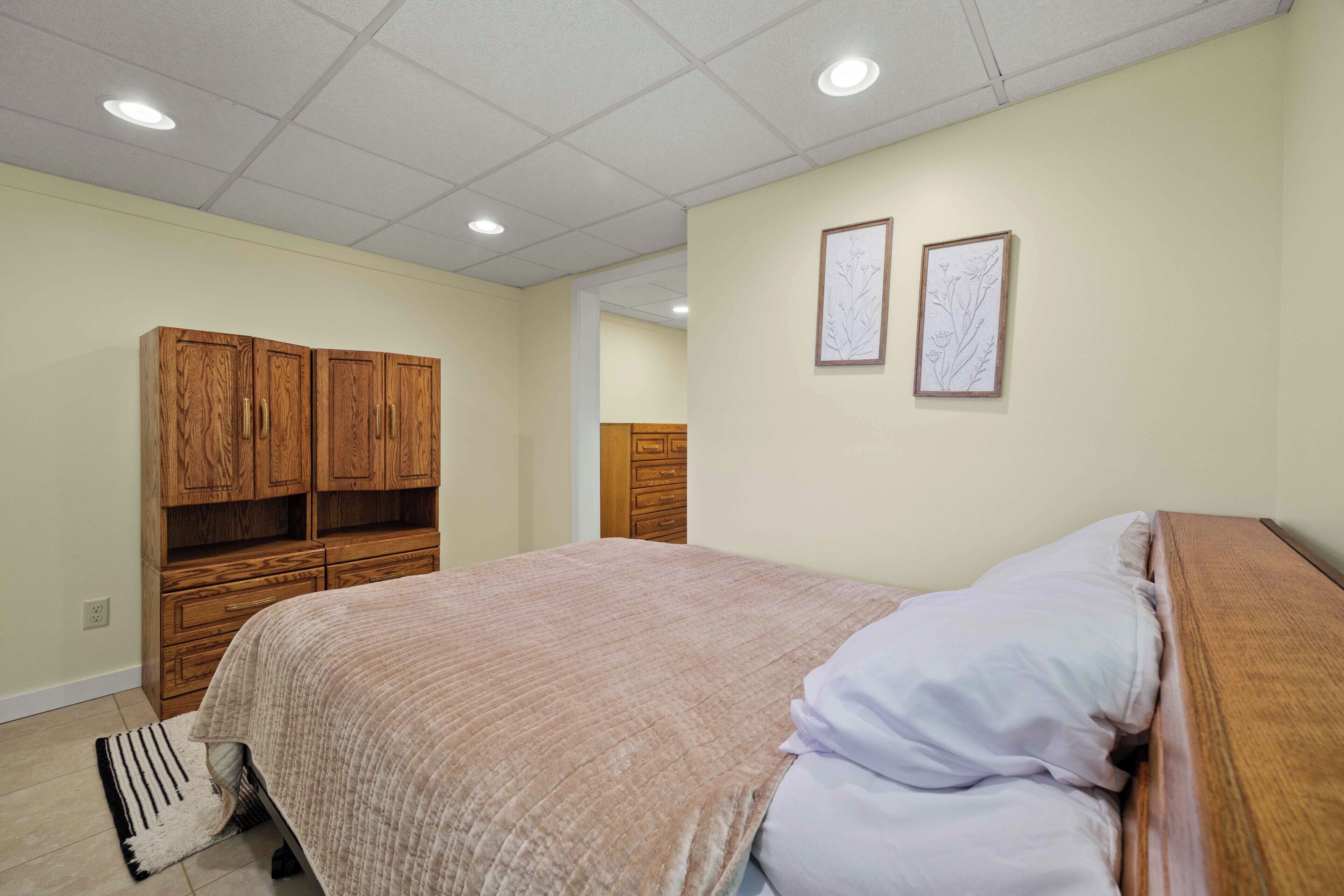 Un dormitorio con cama, armario de madera y dos adornos enmarcados en la pared.