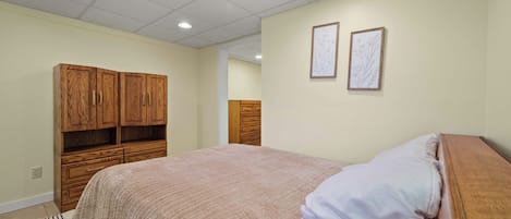 Un dormitorio con cama, armario de madera y dos adornos enmarcados en la pared.