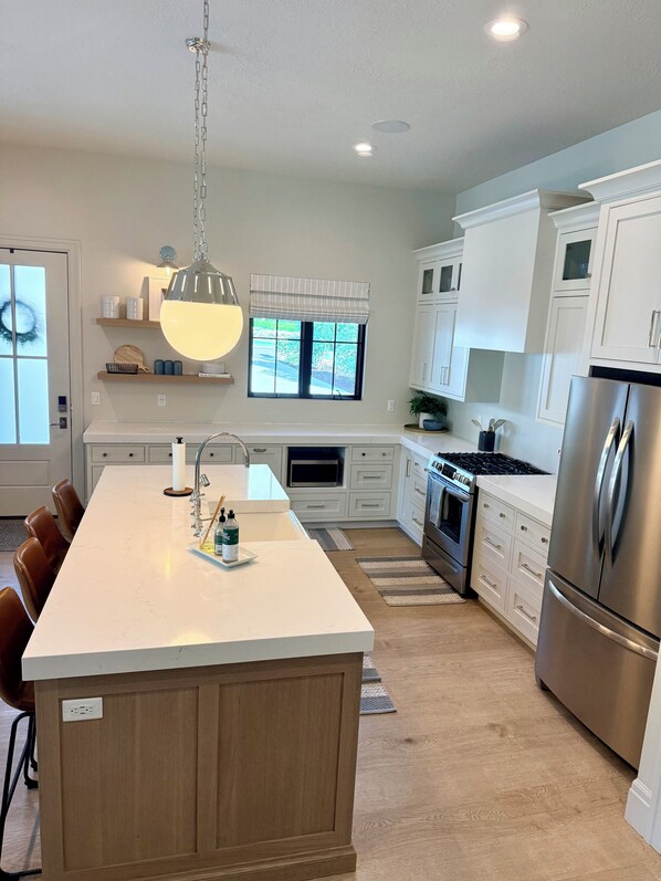 A modern kitchen with a central island, stainless steel appliances, and a large window.