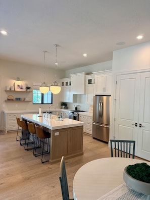 A modern kitchen with a central island, stainless steel appliances, and a dining area with a round table and chairs.