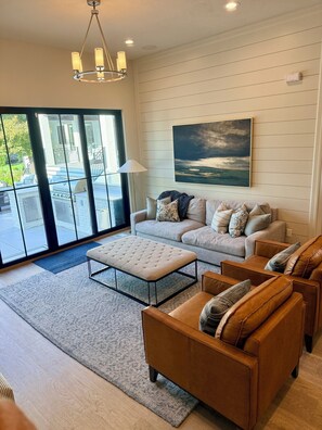 A modern living room with a sofa, ottoman, and leather chairs, a large window with a view, and a painting on the wall.