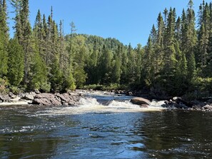 Joki virtaa metsäisen alueen läpi, ja sen varrella on kallioita ja puita.