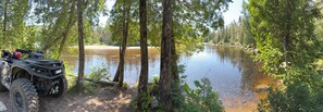 Joki, jonka ympärillä on tiheää metsää, ja joen vasemmalla puolella on pysäköitynä mönkijä.