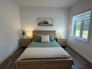 Quarto com cama de madeira, duas mesas de cabeceira com abajures, um quadro na parede e uma janela com vista.